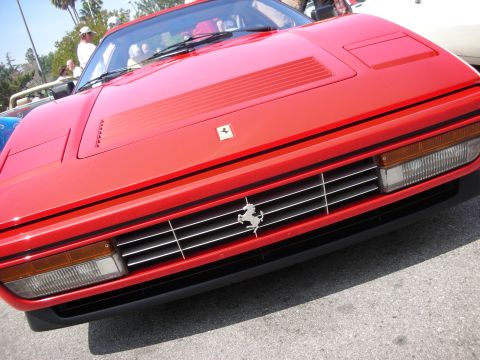 1998 Ford Crown Victoria - Low front-end shot of a red Ferrari showing the yellow prancing-horse emblem, slatted grille and angled pop-up headlight pods.