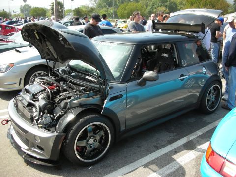 1998 Ford Crown Victoria - grey two-tone MINI Cooper hatchback with its hood raised, exposed engine bay, black wheels and a tall rear wing at a packed car meet.