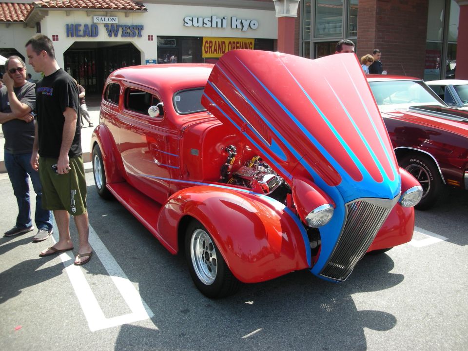 Red 1930s street rod with tilted hood and chrome engine outside Sushi Kyo