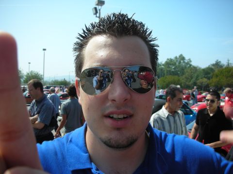 1998 Ford Crown Victoria - Close-up of a young man with spiky hair in a blue polo, mirrored aviator sunglasses reflecting the crowd, at an outdoor car show.