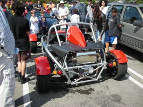 1998 Ford Crown Victoria - red-and-silver exposed tube-frame Ariel Atom track car displayed front-on amid a crowd of onlookers at a car meet.