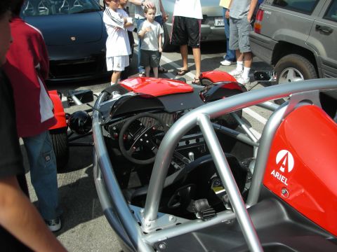 1998 Ford Crown Victoria - Side view of a red exposed-frame Ariel Atom, the 'ARIEL' logo on its rear pod, surrounded by spectators at a car show.