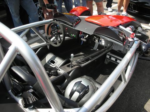 1998 Ford Crown Victoria - open cockpit of a tube-frame Ariel Atom showing the small steering wheel, shifter and a helmet resting on the bucket seat.