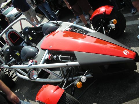 1998 Ford Crown Victoria - Side detail of a red-and-grey Ariel Atom showing the silver tube frame, exposed coil-over shock and a small round gauge.