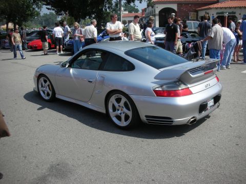 1998 Ford Crown Victoria - Rear three-quarter of a silver Porsche 911 GT2 showing its fixed rear wing and 'GT2' badge, surrounded by spectators at a meet.