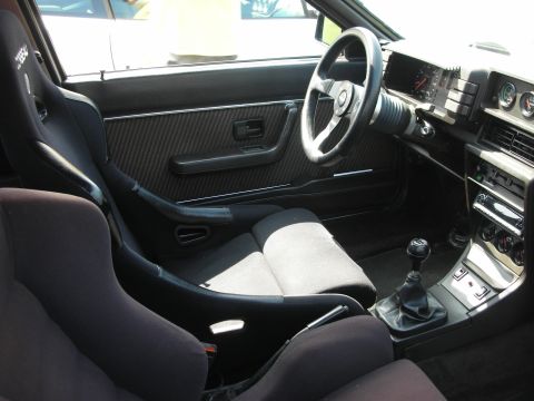 1998 Ford Crown Victoria - Interior of a sporty coupe showing a black bucket seat, carbon-look door panel, aftermarket steering wheel and exposed manual shifter.
