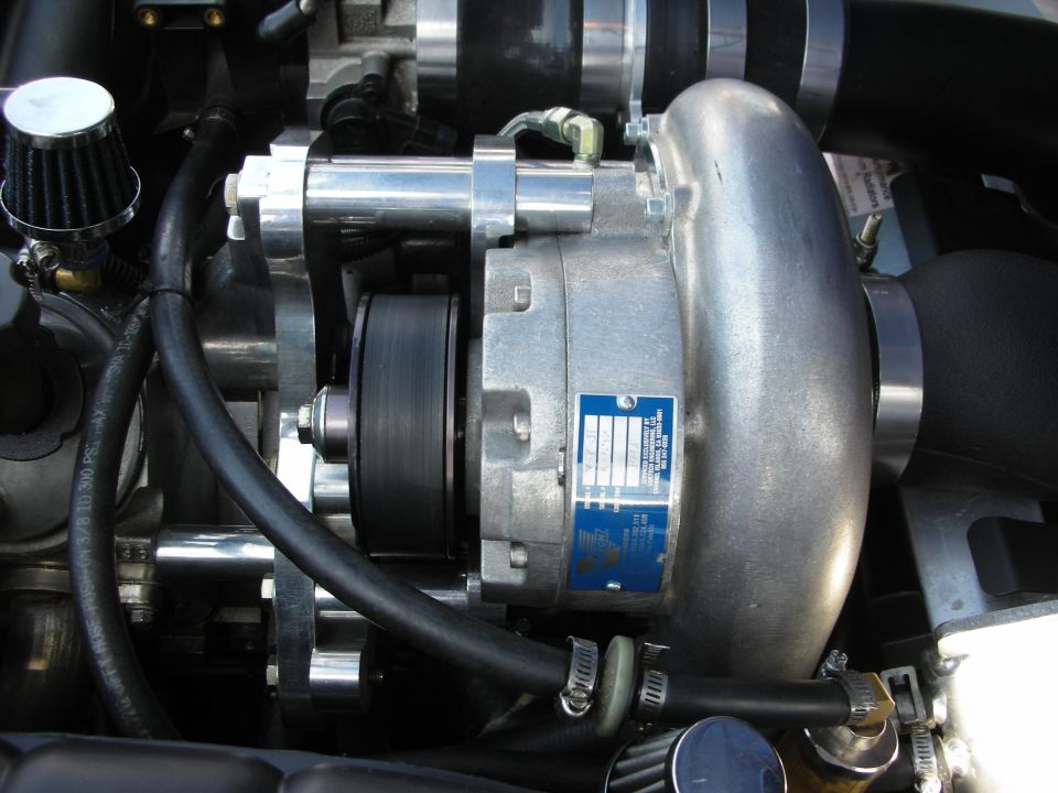 Close-up of a belt-driven supercharger with blue ID label in an engine bay