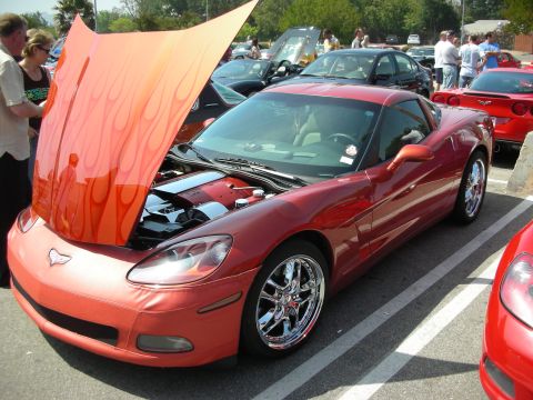 1998 Ford Crown Victoria - copper Chevrolet Corvette coupe with a flame-painted underside hood propped open in a crowded car-show lot.