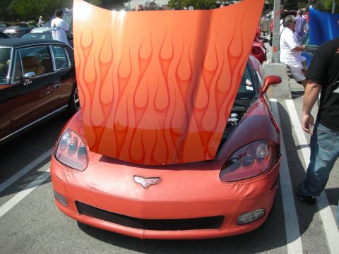 1998 Ford Crown Victoria - front of an orange Corvette with its flame-painted hood raised, parked among cars with a person standing beside it.
