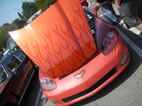 1998 Ford Crown Victoria - low-angle view of an orange Corvette with a flame-painted hood raised, parked in a sunny car-show lot.