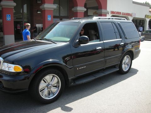 1998 Ford Crown Victoria - black Lincoln Navigator SUV on chrome wheels parked in front of a Hooper Camera storefront.