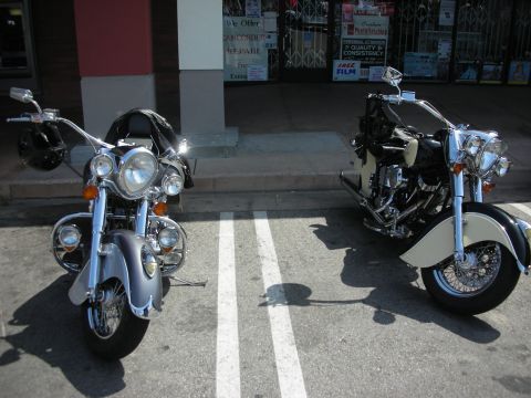1998 Ford Crown Victoria - Two chrome-and-black cruiser motorcycles with large round headlights parked diagonally on a sunny street.