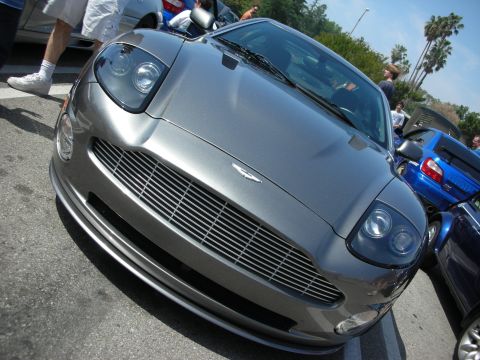 1998 Ford Crown Victoria - low front view of a gray Aston Martin coupe showing its winged badge and slatted grille under sunlight.
