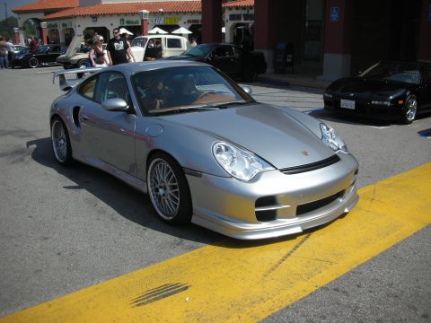 1998 Ford Crown Victoria - silver Porsche 911 coupe with a front lip and rear wing parked at the edge of a car-show lot.