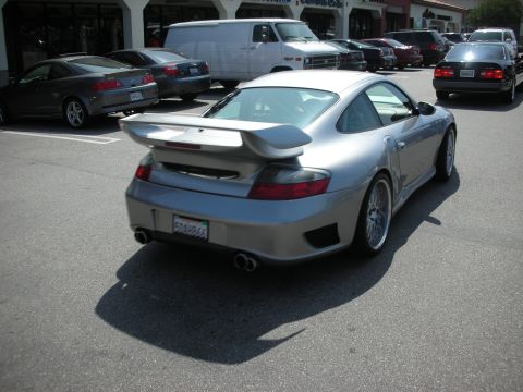 1998 Ford Crown Victoria - rear three-quarter of a silver Porsche 911 with a raised wing and twin exhausts in a parking lot.