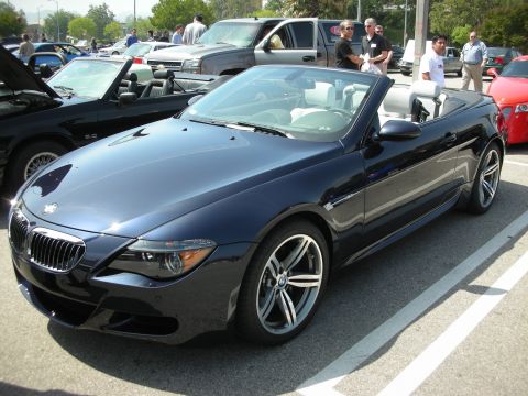 1998 Ford Crown Victoria - dark blue BMW M6 convertible with the top down, parked among cars with onlookers standing nearby.