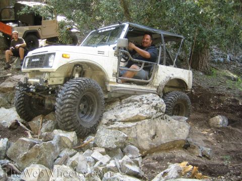 1987 Suzuki Samurai - A white 1987 Suzuki Samurai tackles a challenging rocky trail with another vehicle visible in the background.