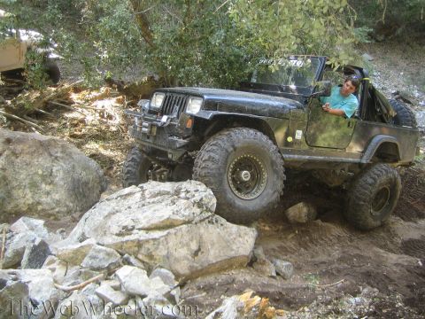 1987 Suzuki Samurai - A black Jeep Wrangler maneuvers through a challenging rocky terrain, with another vehicle partially visible in the background.