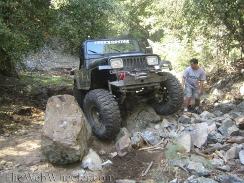 1987 Suzuki Samurai - A black Jeep Wrangler tackles a challenging off-road course with large tires and a winch.