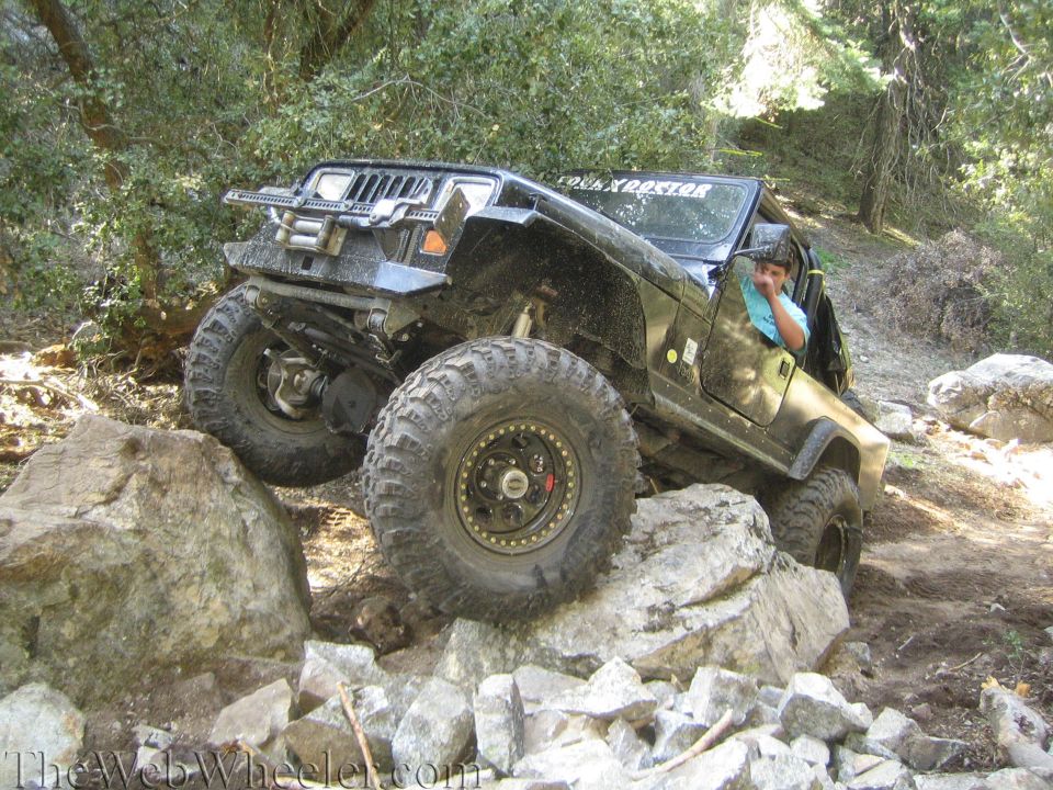 Black Jeep Wrangler climbing over large rocks on a dirt trail