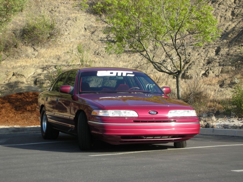 Maroon 1992 Ford Crown Victoria parked in a lot with a tree and dry hillside behind it