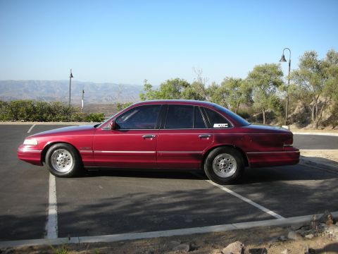 1992 Ford Crown Victoria - A red 1992 Ford Crown Victoria is parked in a lot on a sunny day with a sticker on the rear quarter panel.