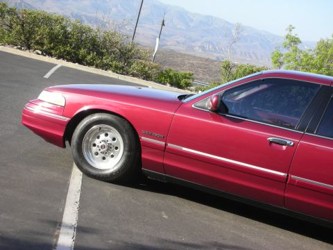 1992 Ford Crown Victoria - A red 1992 Ford Crown Victoria sedan is parked on an asphalt surface with a mountainous landscape in the background.