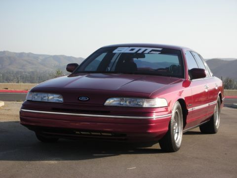 1992 Ford Crown Victoria - A maroon 1992 Ford Crown Victoria is parked on a paved surface with a mountainous landscape behind it.