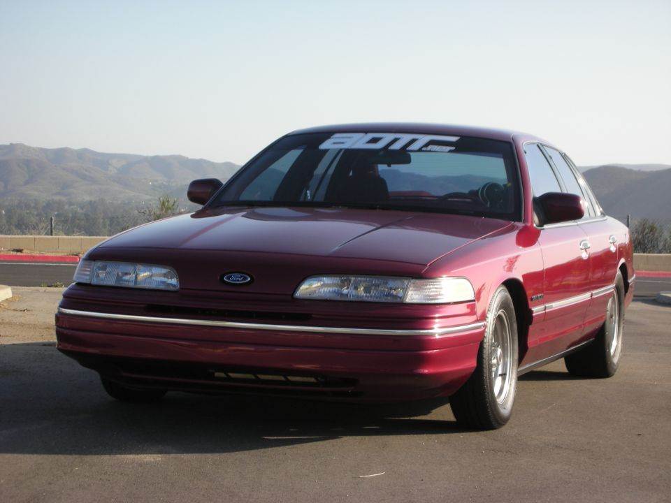 Maroon 1992 Ford Crown Victoria parked outside with mountains in the background. Banner on windshield reads 'BDM'