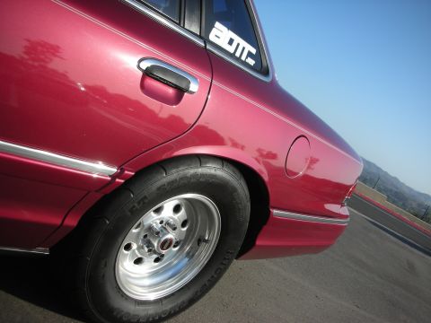 1992 Ford Crown Victoria - Rear quarter panel view of a red sedan with drag tires and custom wheels, a 'BOTM' sticker on the rear window.
