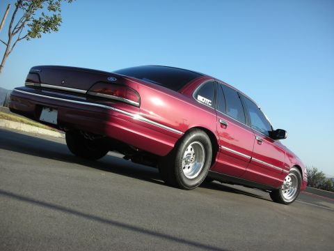 1992 Ford Crown Victoria - A red 1992 Ford Crown Victoria is shown from a low angle, highlighting its modified wheels and tires.