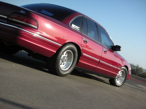1992 Ford Crown Victoria - A red 1992 Ford Crown Victoria is shown from a low angle, highlighting its modified suspension and drag racing tires.