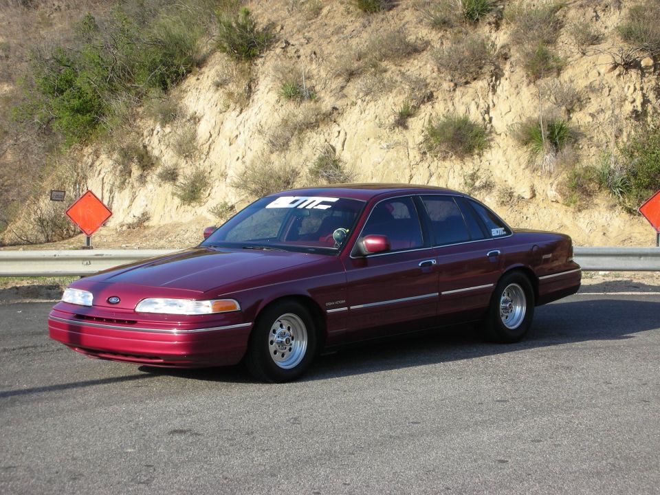 Maroon Ford Crown Victoria sedan, 3/4 front view on a canyon road