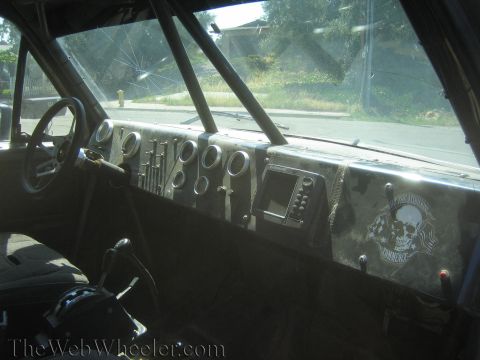 1990 Ford Bronco - race truck dashboard with a cluster of round gauges, a screen and a skull-graphic panel, viewed through the windshield.