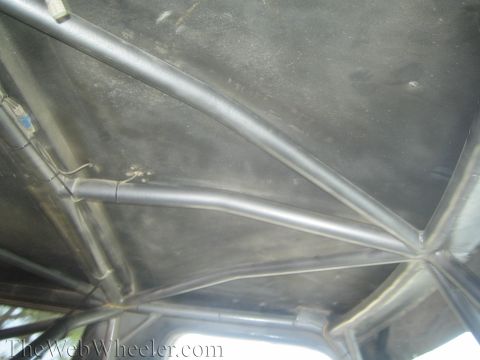 1990 Ford Bronco - Looking up at the headliner of a vehicle showing a welded tubular steel roll cage spanning the roof.