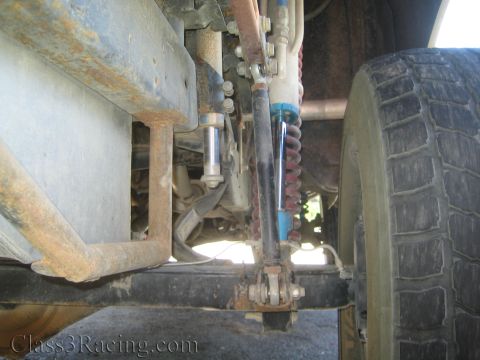1990 Ford Bronco - Underbody shot of a truck showing the frame rail, steering linkage, and a blue coilover shock beside a worn off-road tire.