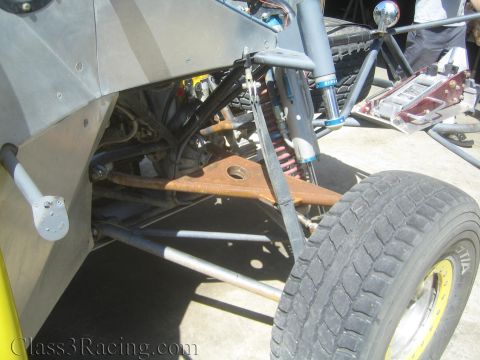 1990 Ford Bronco - Close-up of a tube-chassis off-road race vehicle's front suspension with A-arms, coilover shock, and a racing tire.