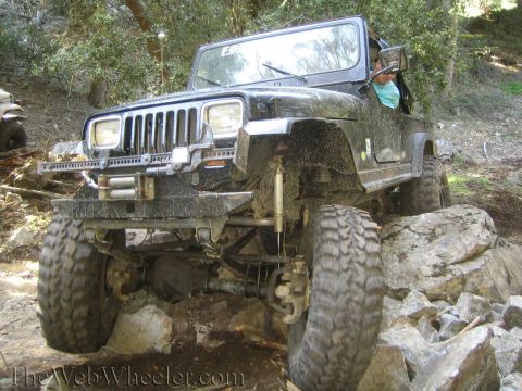 1987 Suzuki Samurai - Jeep Wrangler tackling a challenging off-road course with large rocks and steep inclines.