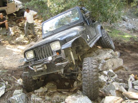 1987 Suzuki Samurai - A black Jeep Wrangler navigates a rocky off-road trail, with another vehicle in the background.