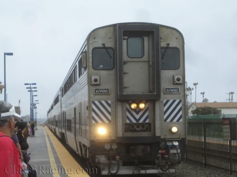 1990 Ford Bronco - stainless-steel commuter rail car numbered 6900 pulls up to a station platform as people wait on the platform.