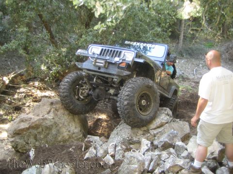 1987 Suzuki Samurai - A heavily modified Jeep Wrangler navigates a rocky trail with a person watching.