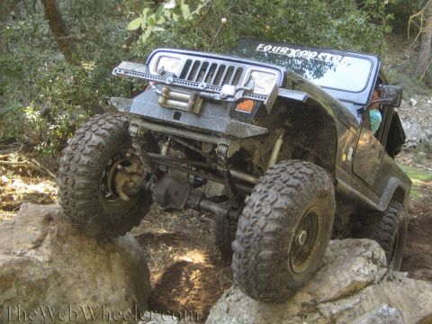 1987 Suzuki Samurai - A black Jeep Wrangler navigates a rocky trail, demonstrating its off-road capabilities with large tires and a lifted suspension.