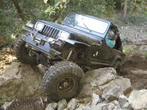 1987 Suzuki Samurai - Jeep Wrangler tackling difficult terrain on a rocky path.