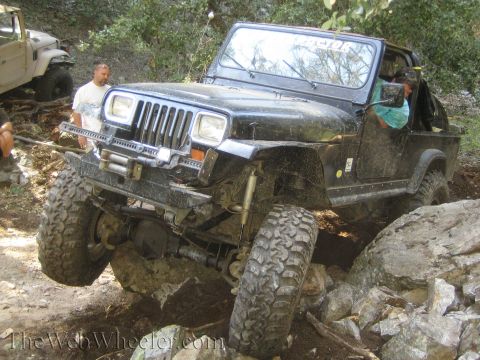 1987 Suzuki Samurai - A black Jeep Wrangler TJ is shown off-roading over large rocks, with another vehicle visible in the background.