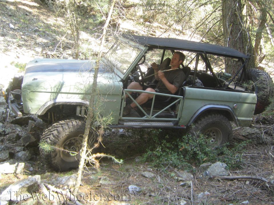 Green Ford Bronco with roll cage and off-road tires navigating rocky terrain