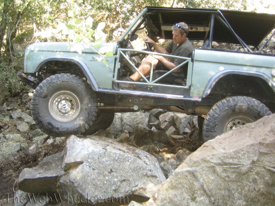 Off-road vehicle with roll cage and removed doors navigating rocky terrain