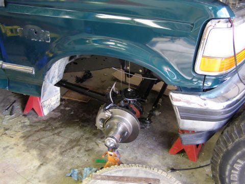 1993 Ford Bronco - Front wheel assembly of a green SUV, likely from the early 1990s, is elevated on jack stands for maintenance.