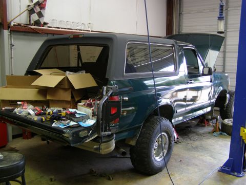 1993 Ford Bronco - This green SUV is in a garage with its tailgate open, revealing boxes and tools, and the hood is up.