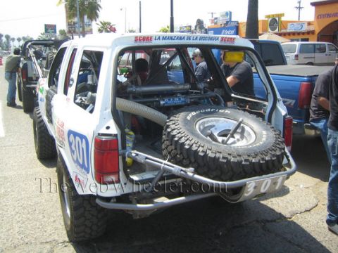 1992 Ford Explorer - This modified SUV, possibly a Ford Explorer, is equipped for off-road racing with a prominent spare tire and racing numbers.