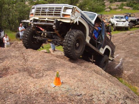 1986 Ford Bronco - Modified Ford Bronco navigates a rocky incline with other vehicles in the background.
